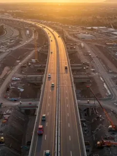 Modern highway construction in Mexico with cranes and construction vehicles at sunset.