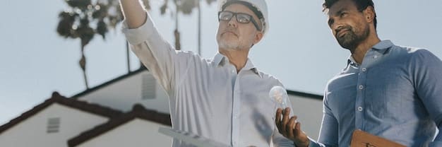 Two construction executives, one American and one Mexican, shaking hands firmly in front of a blueprint, symbolizing a successful joint venture in the construction industry.
