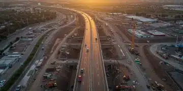 Modern highway construction in Mexico with cranes and construction vehicles at sunset.